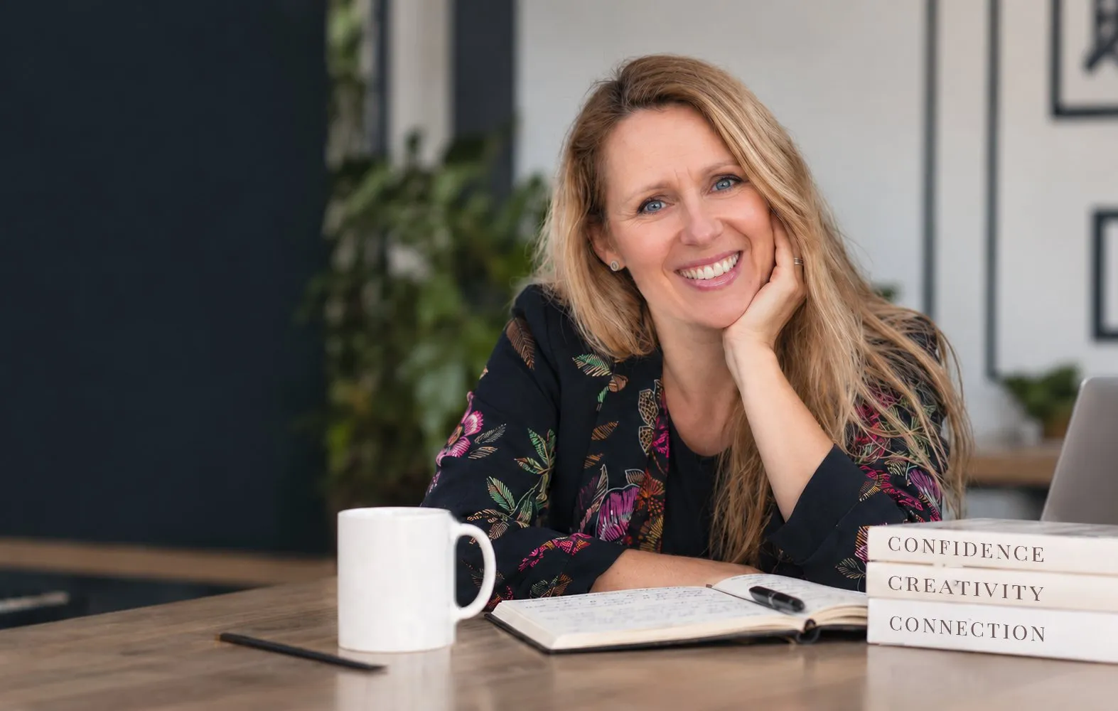 Kirsten at her desk, wide, warm, looking at camera